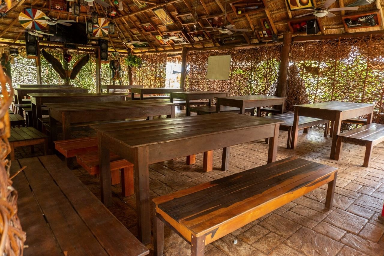 Mesas y bancas largas de madera bajo una palapa